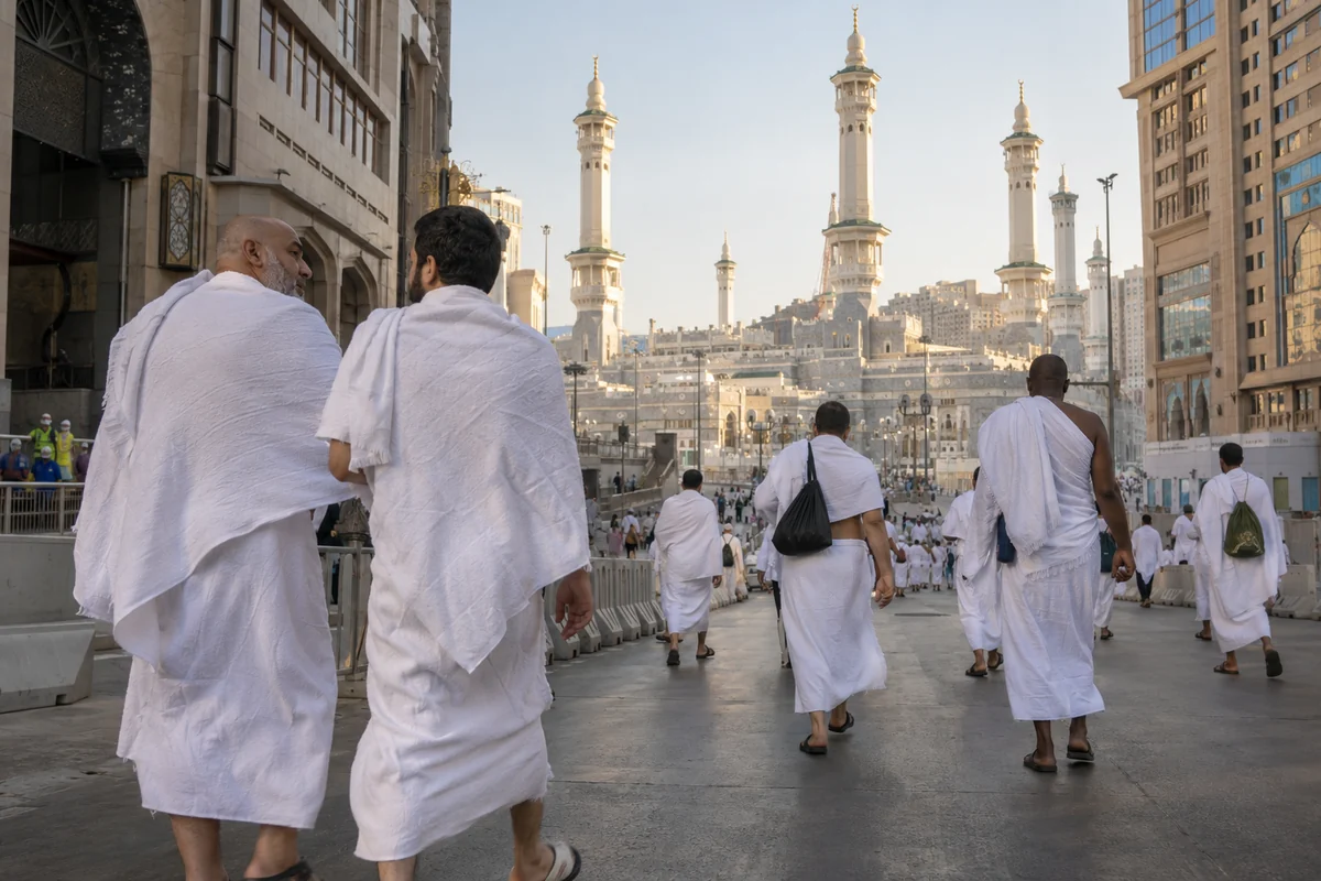 Two men in ihram walking along a street towards a mosque's minarets, seen from behind
