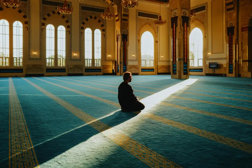 A worshipper praying in a sunlit mosque